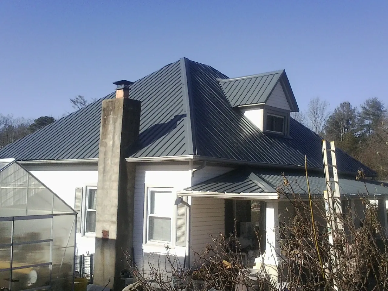 Dark blue standing seam metal roof on a white farmhouse with dormer — Slate & Tile Roof Repair by Roofing Brothers in Anaconda