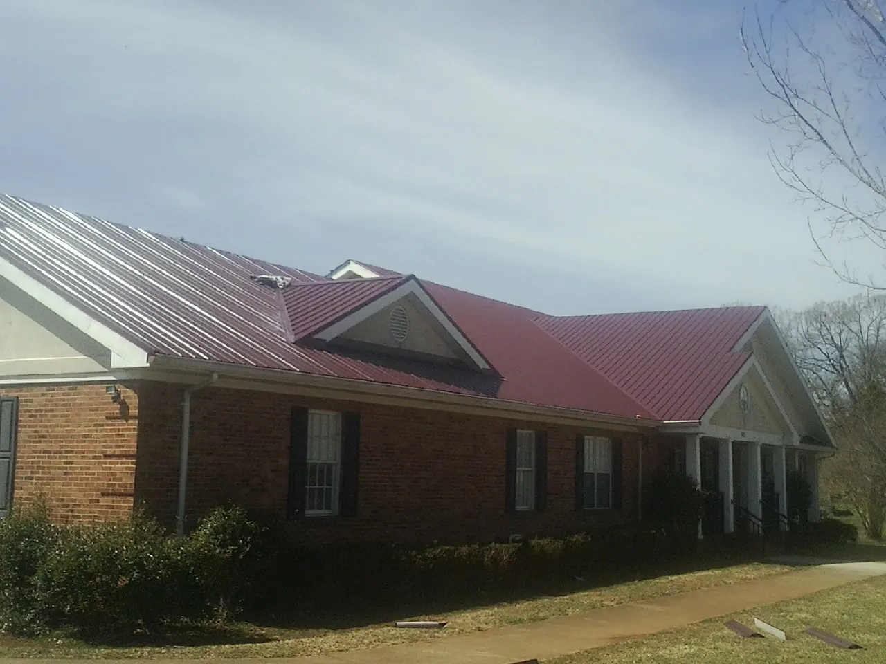 Red metal roof with gabled entries on a long brick building, from a Hail Damage Roof Repair job in Anaconda