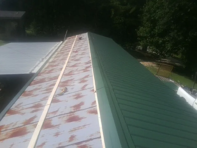 Old rusted panels beside newly installed green metal roofing — Wind Damage Roof Repair by Roofing Brothers in Anaconda