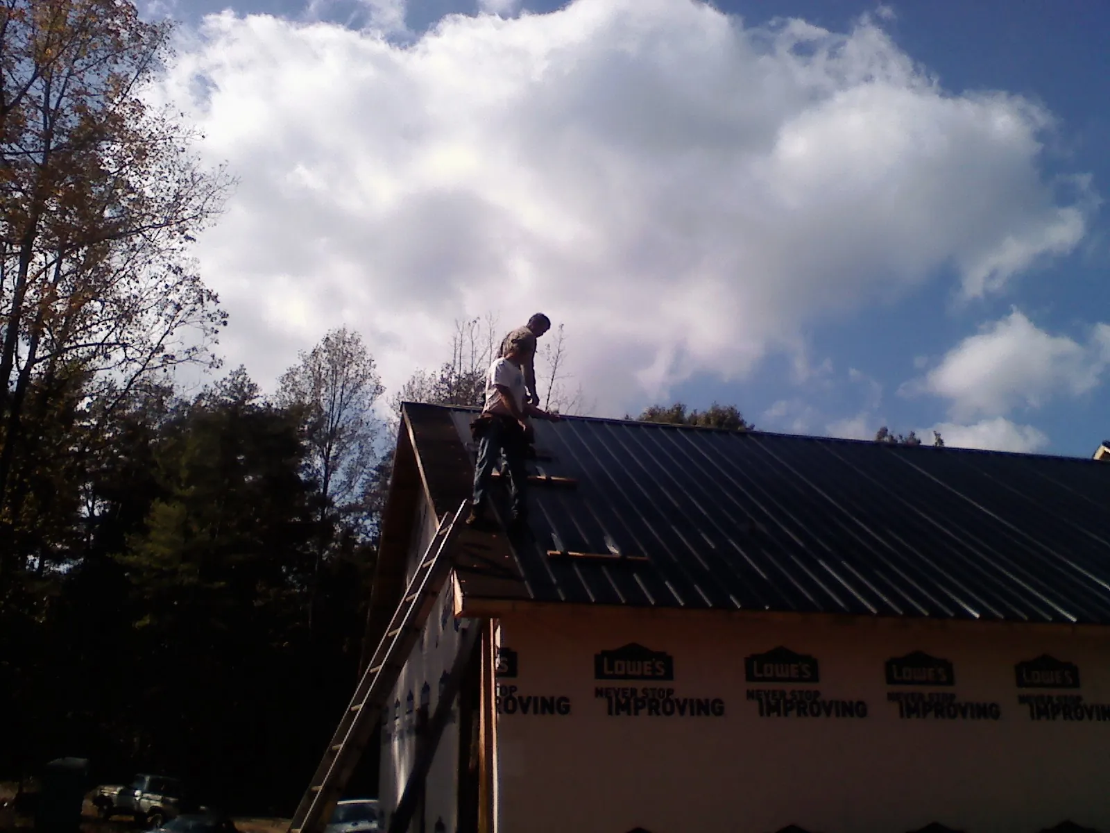 Roofer fastening dark metal panels high against a cloudy sky, from a Roof Inspection job in Anaconda
