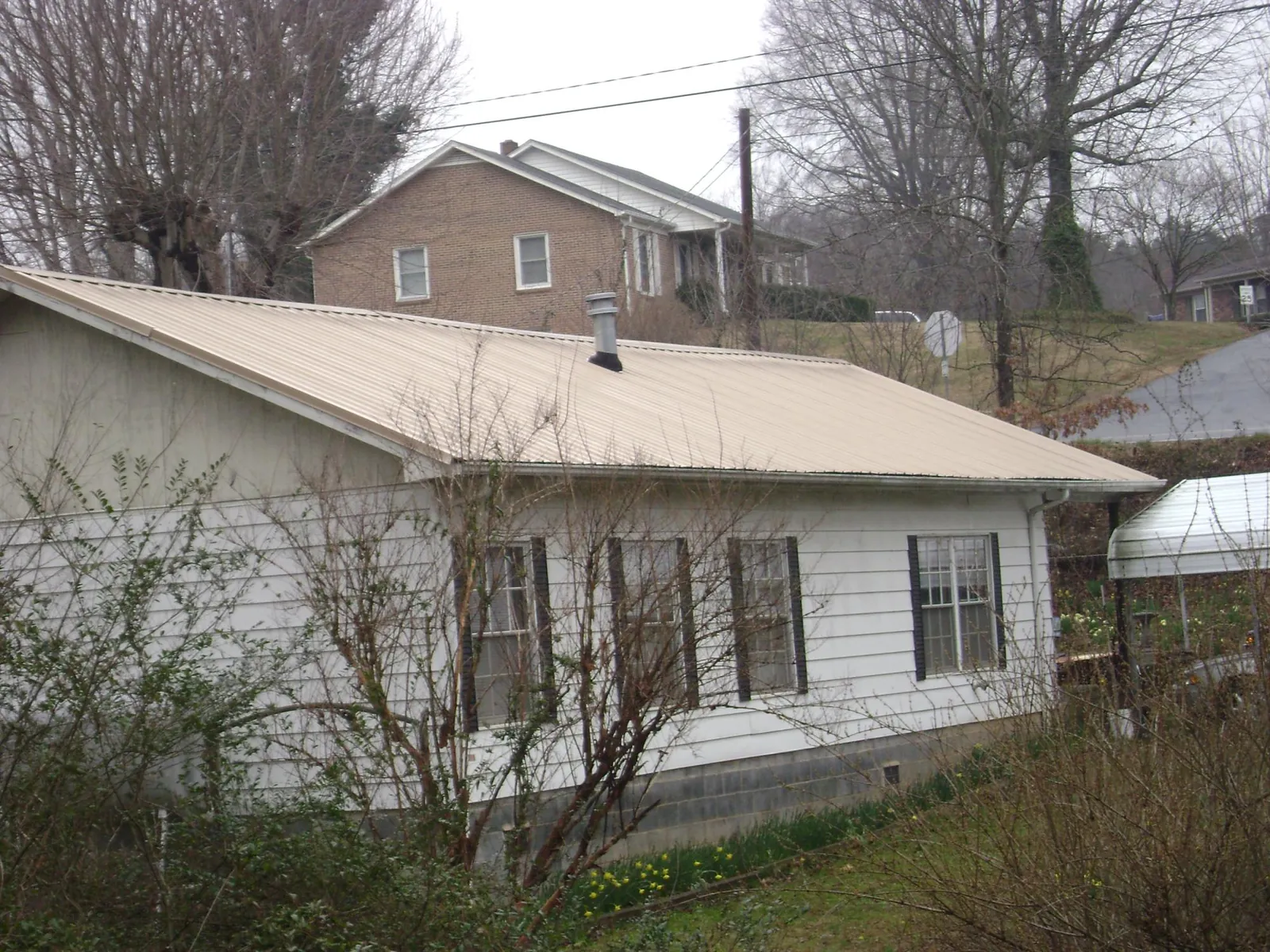 Tan metal roof on a white sided house set into a hillside — Commercial Roofing by Roofing Brothers in Anaconda